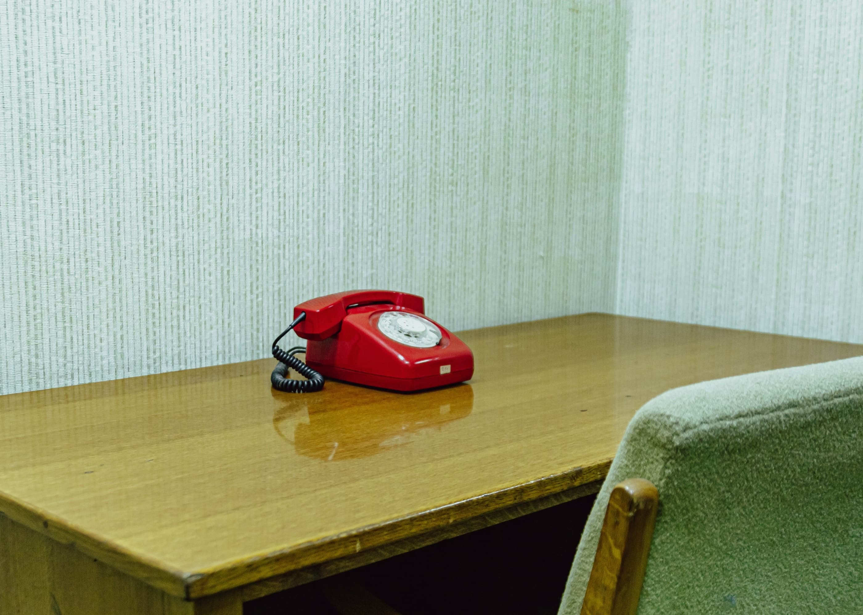 A red rotary phone waiting on a wooden desk